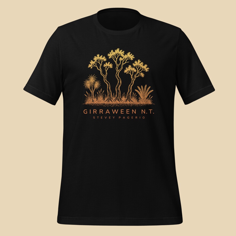 Front of a black t-shirt printed with the Girraween N.T. design: three gum trees with pandanus, cycad and spear grass above the words GIRRAWEEN N.T. and STEVEY PAGERIO, in a yellow-to-orange fade